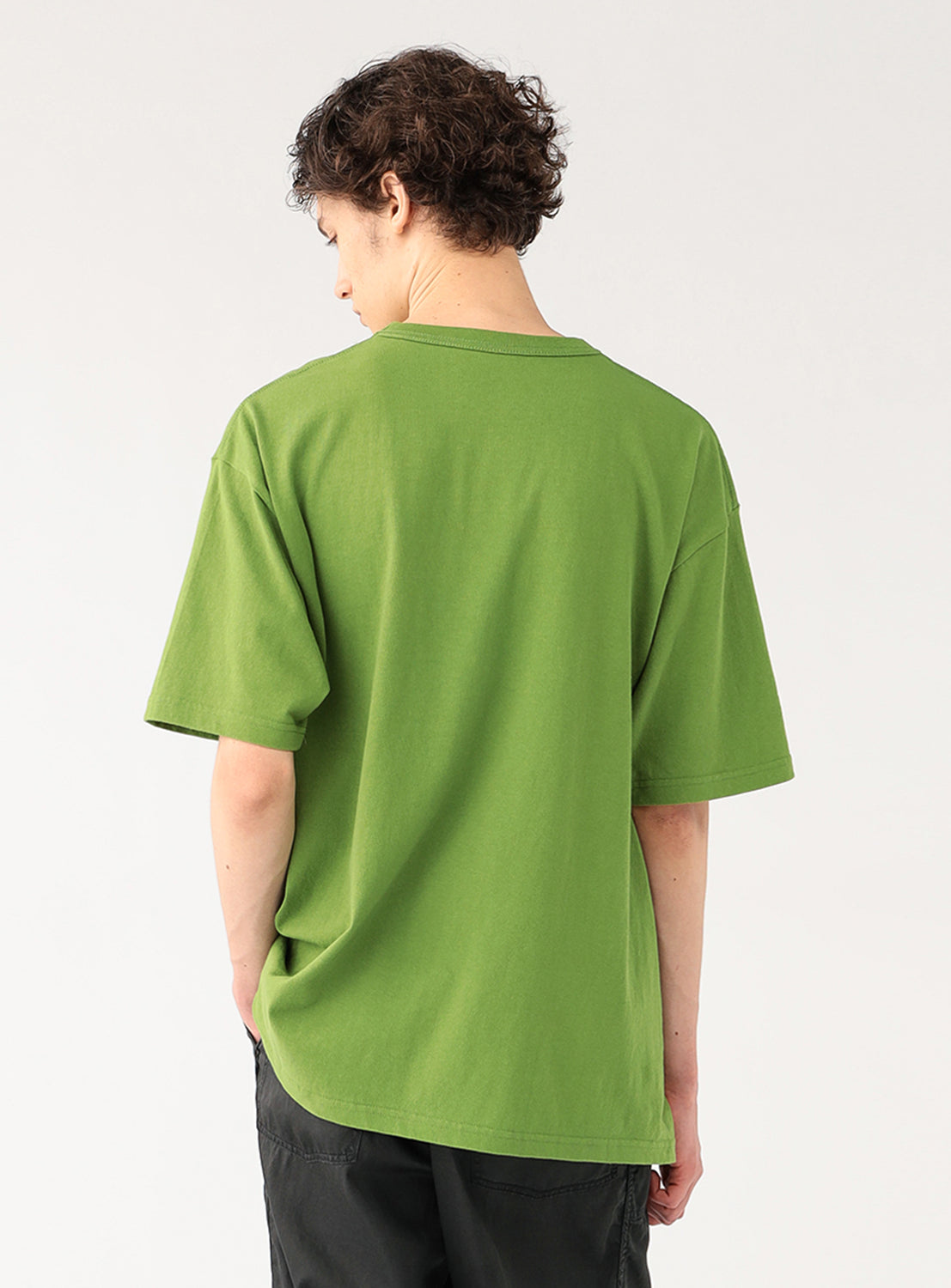 Model wearing a kelly green plain t-shirt and dark pants, back view, highlighting the shirt's smooth fabric.