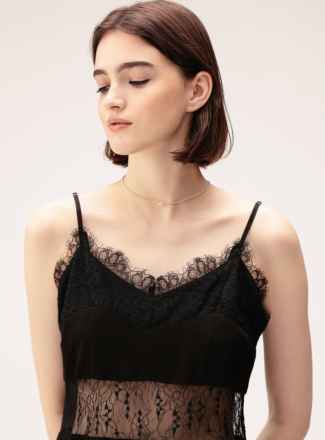 A woman with short brown hair wears a black lace dress and the Ray BEAMS Silver Top Leather Choker, gazing downward with a neutral expression against a plain light background.