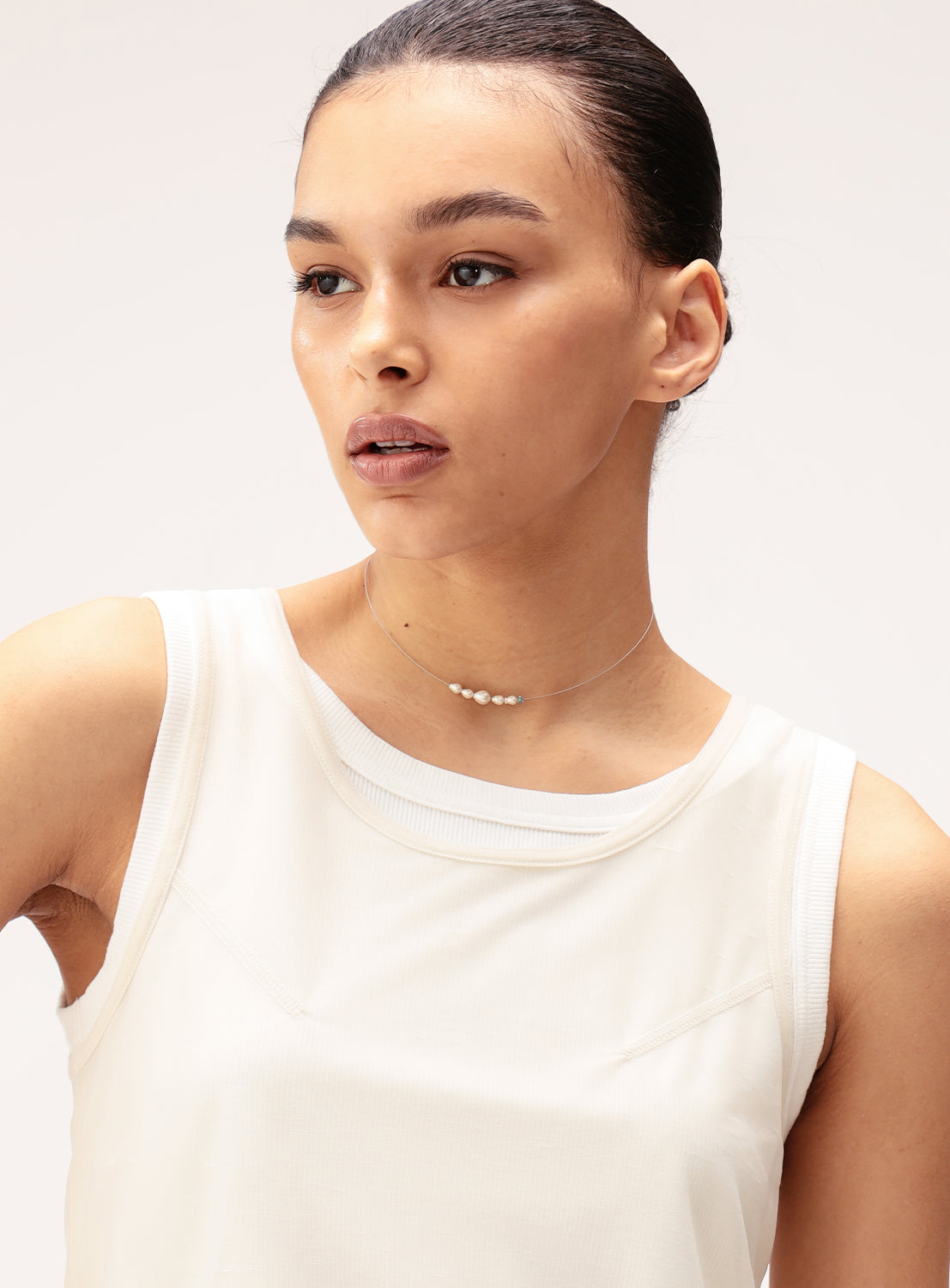 A woman wearing a sleeveless white top and the Ray BEAMS Glass Pearl and Delicate Wire Necklace gazes slightly to the side against a plain light background.