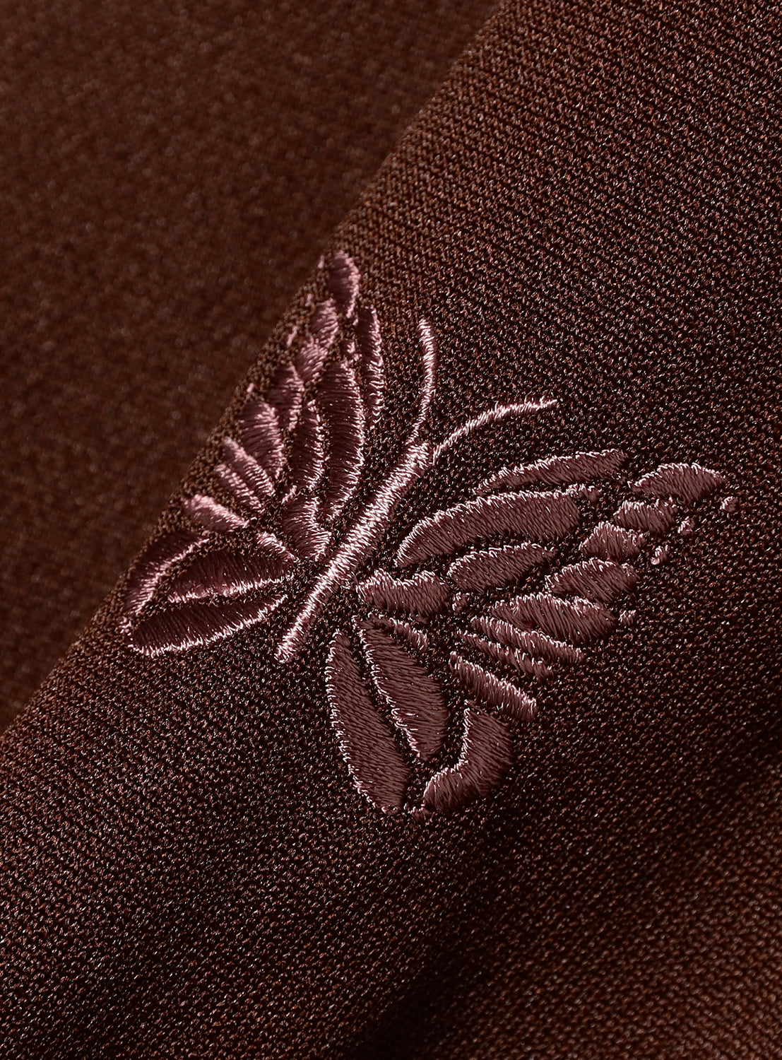 Close-up of a brown/burgundy fabric with an embroidered butterfly design.