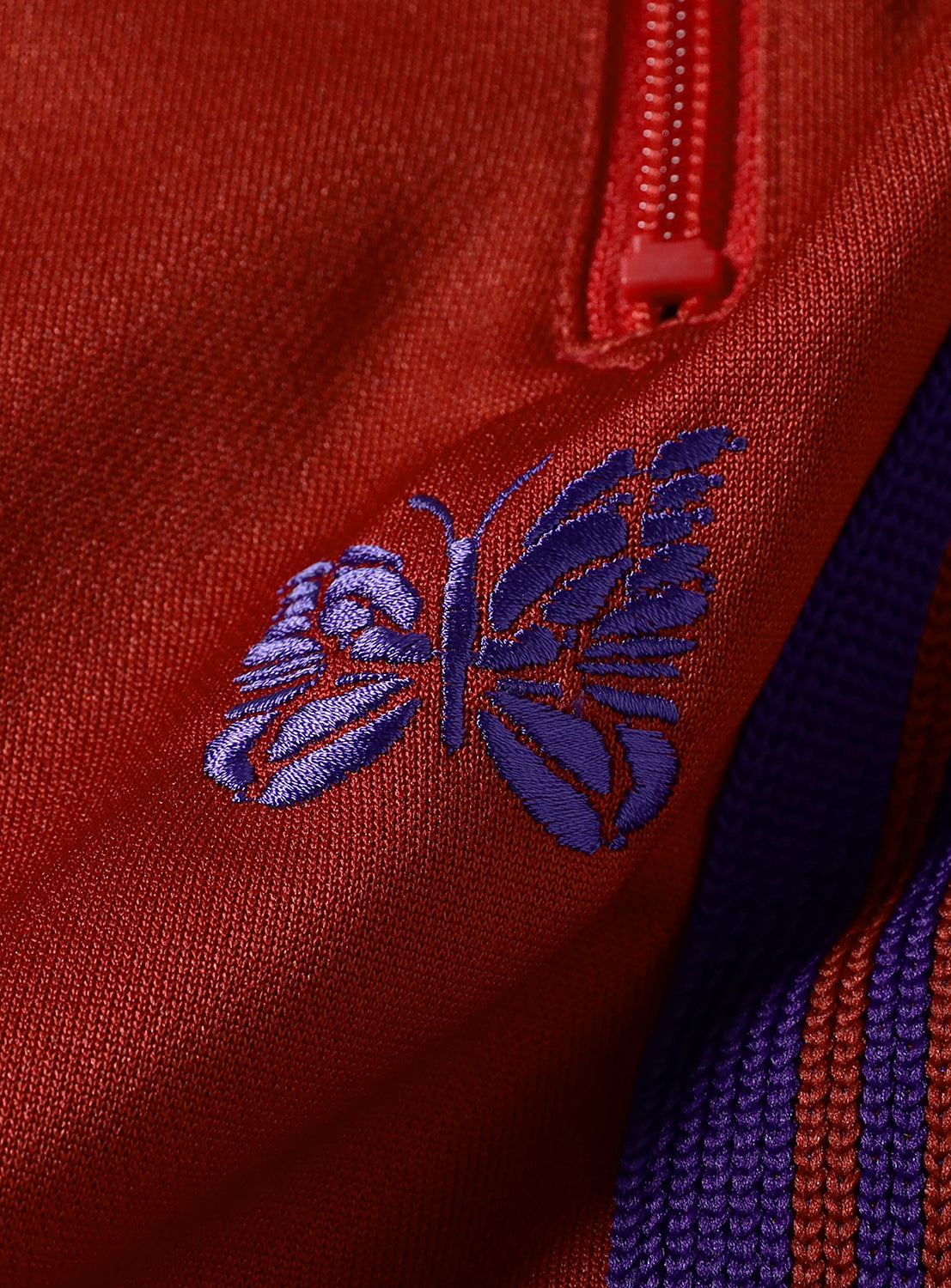 Close-up of a red fabric with a purple embroidered butterfly.