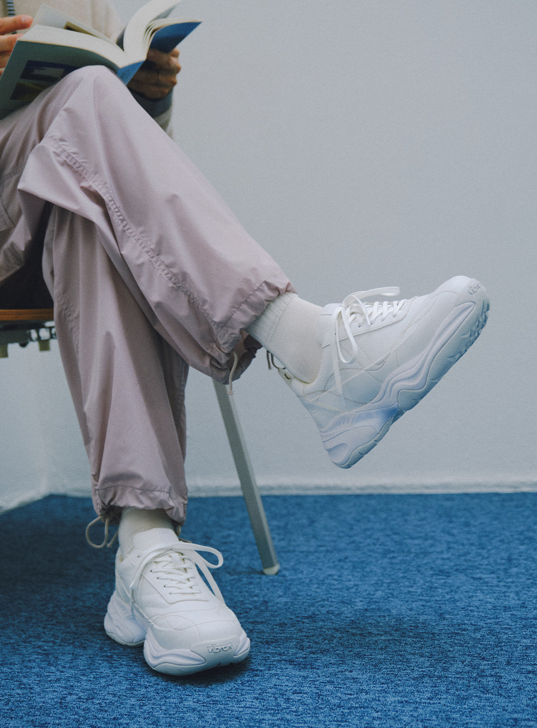 Close-up of a person wearing white chunky sneakers, with the foot propped up.