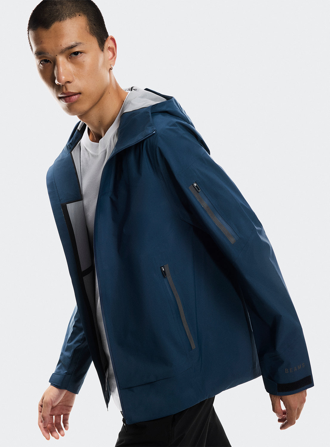 Side view of a model wearing a blue trek zip-up jacket with multiple zippers highlighting the movement of the jacket. 