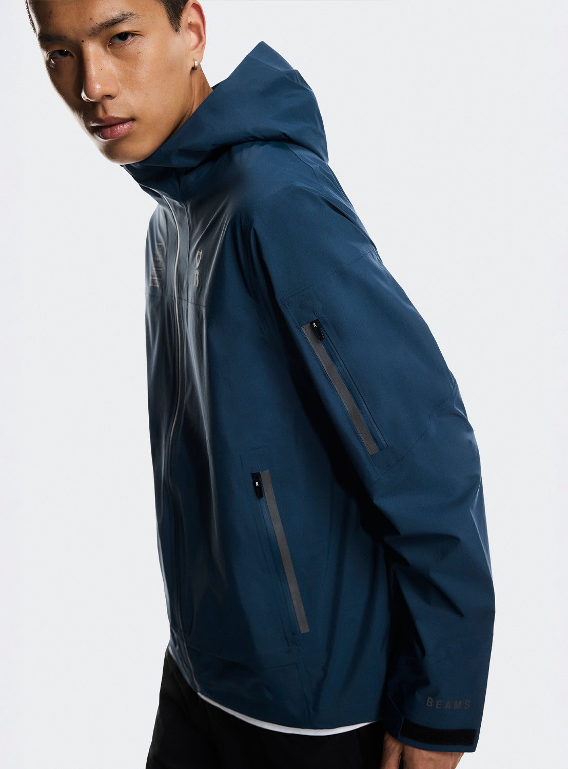 Side view of a model wearing a blue trek zip-up jacket with zipper on the sleeve and side. 
