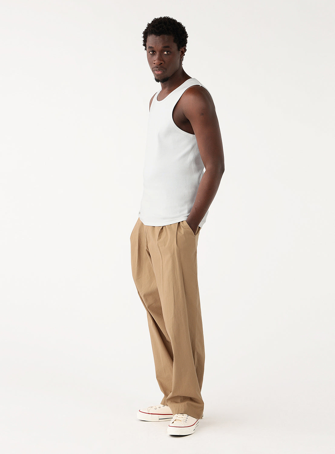Profile view of a model wearing a white ribbed tank top, highlighting the garment's cut.