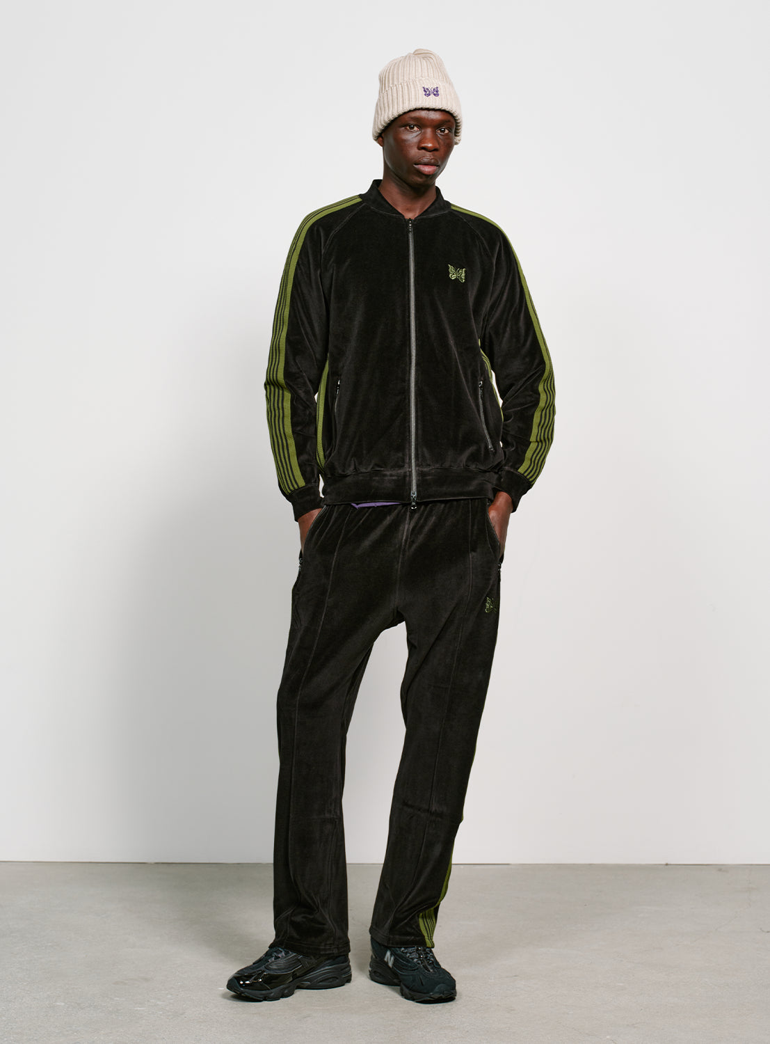 Model wearing a black velour jacket with bright green stripes on the sleeves and side, with the matching pants. 
