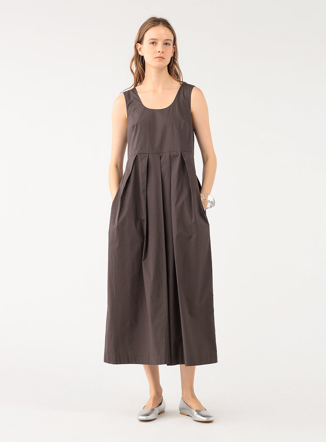 Full body shot of a model wearing a brown sleeveless jumpsuit, styled with silver flats.