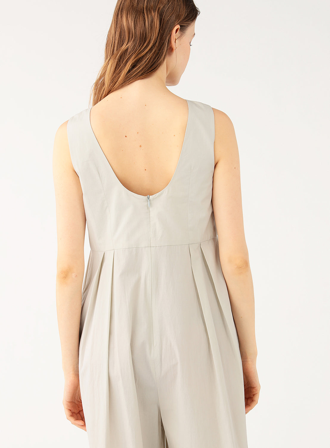 Close up of model wearing a 100% cotton wide-leg jumpsuit, back view, highlighting the relaxed fit and back pleat details.