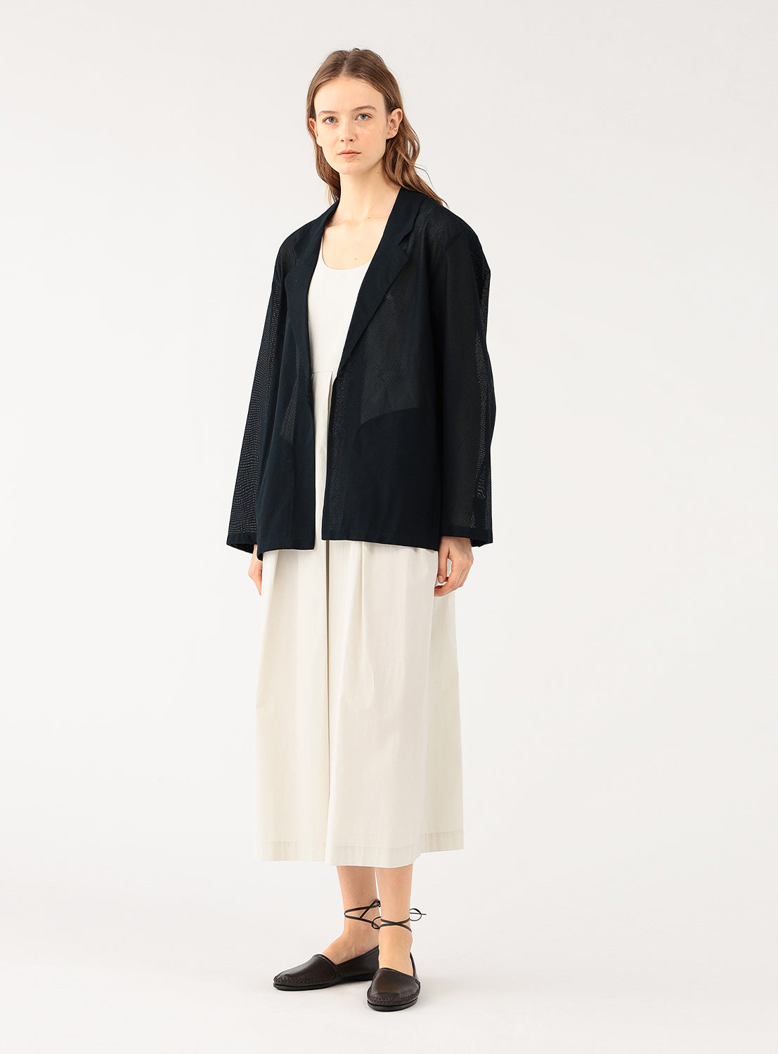 A female model wearing a dark navy blue open blazer over a light top and cream-colored wide-leg pants, standing full body.