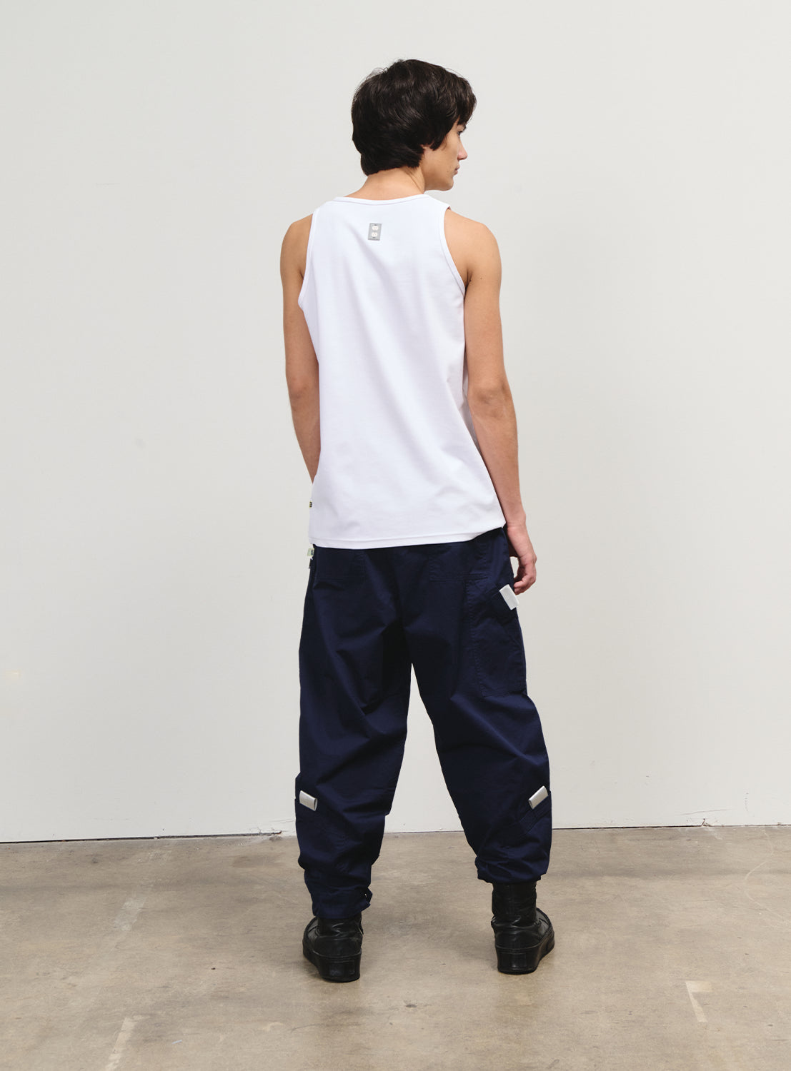 Back view of a model in a white tank top, highlighting the back silhouette and small graphic detail.