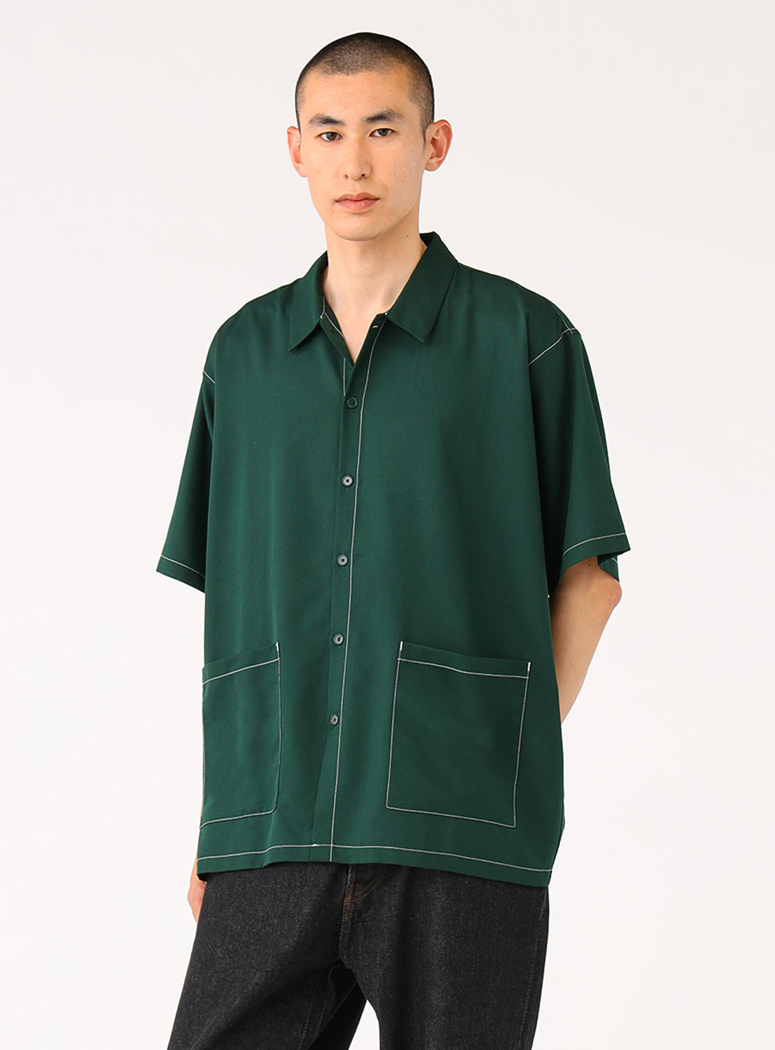 Front-facing model wearing the dark green BEAMS Stitching Easy Shirt, designed with a streamlined, minimalist aesthetic and accented by a generously sized waist pocket and subtle tonal stitching. 