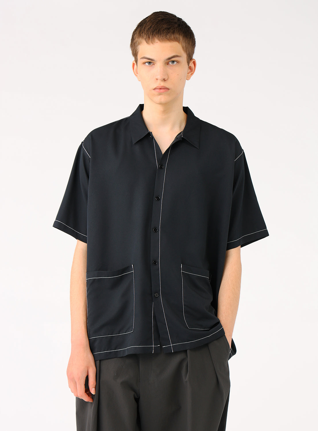 Model facing forward wearing the black BEAMS Stitching Easy Shirt, featuring a clean, minimalist design with discreet color-matched stitching and a large oversized waist pocket. 