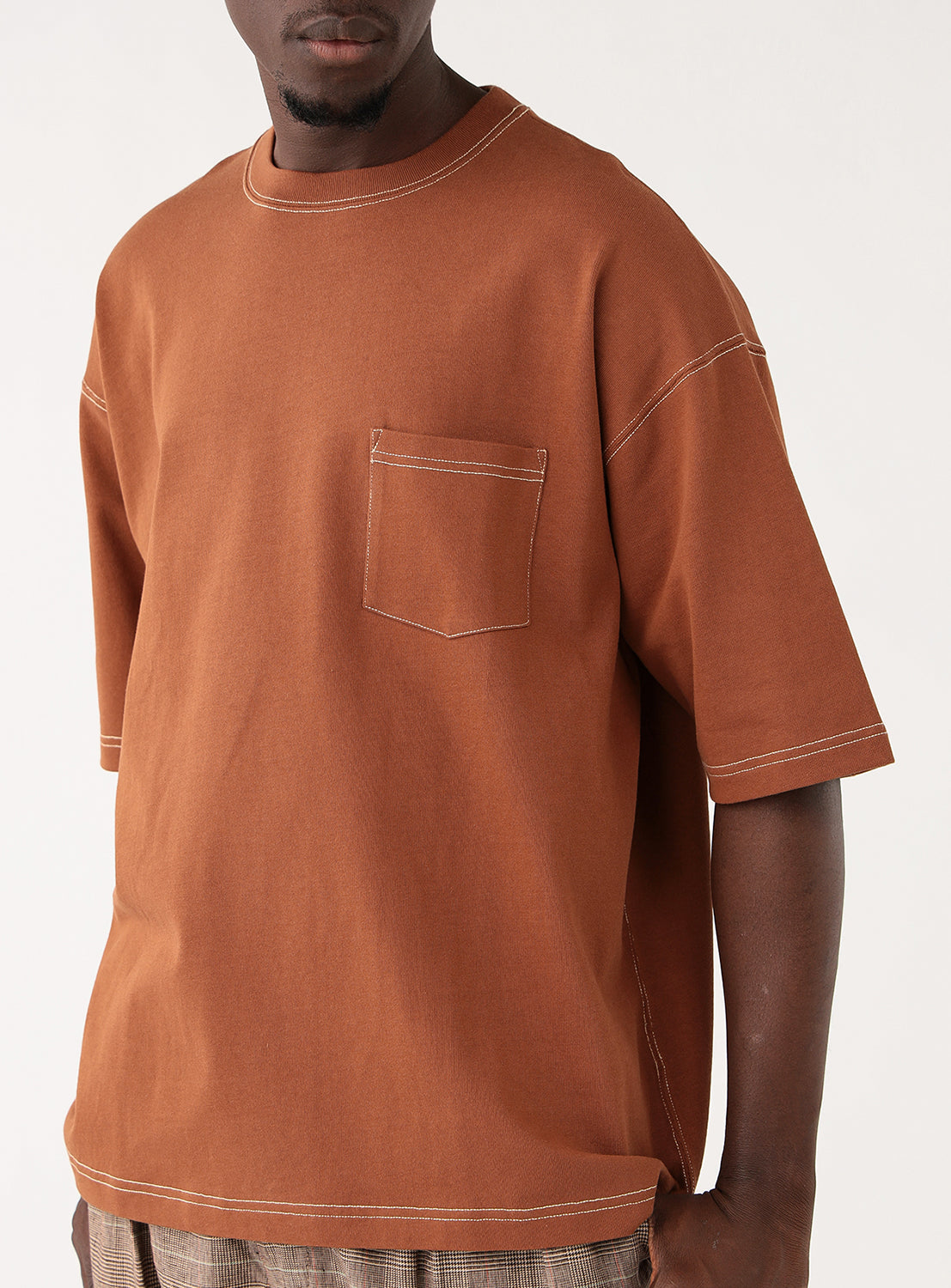 Close-up of a model wearing the brown t-shirt, focusing on the chest pocket and contrast stitching detail.