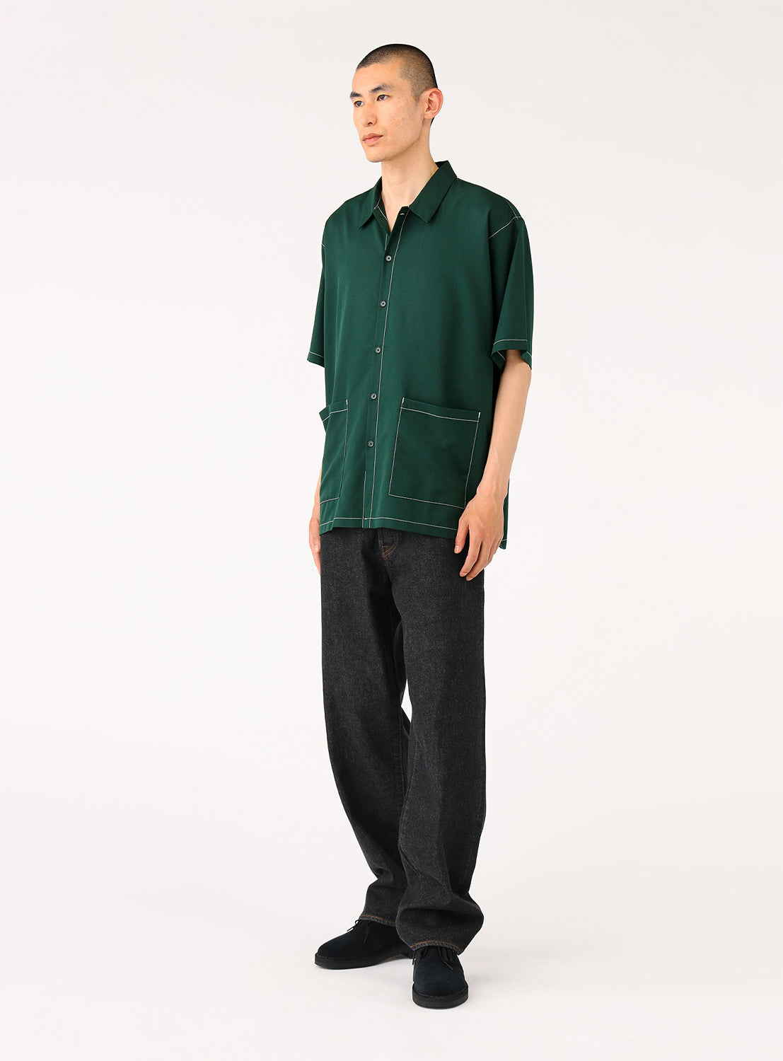 Quarter-angle view of model wearing the dark green BEAMS Stitching Easy Shirt, showcasing its minimalist design with subtle tonal stitching and a large oversized waist pocket.