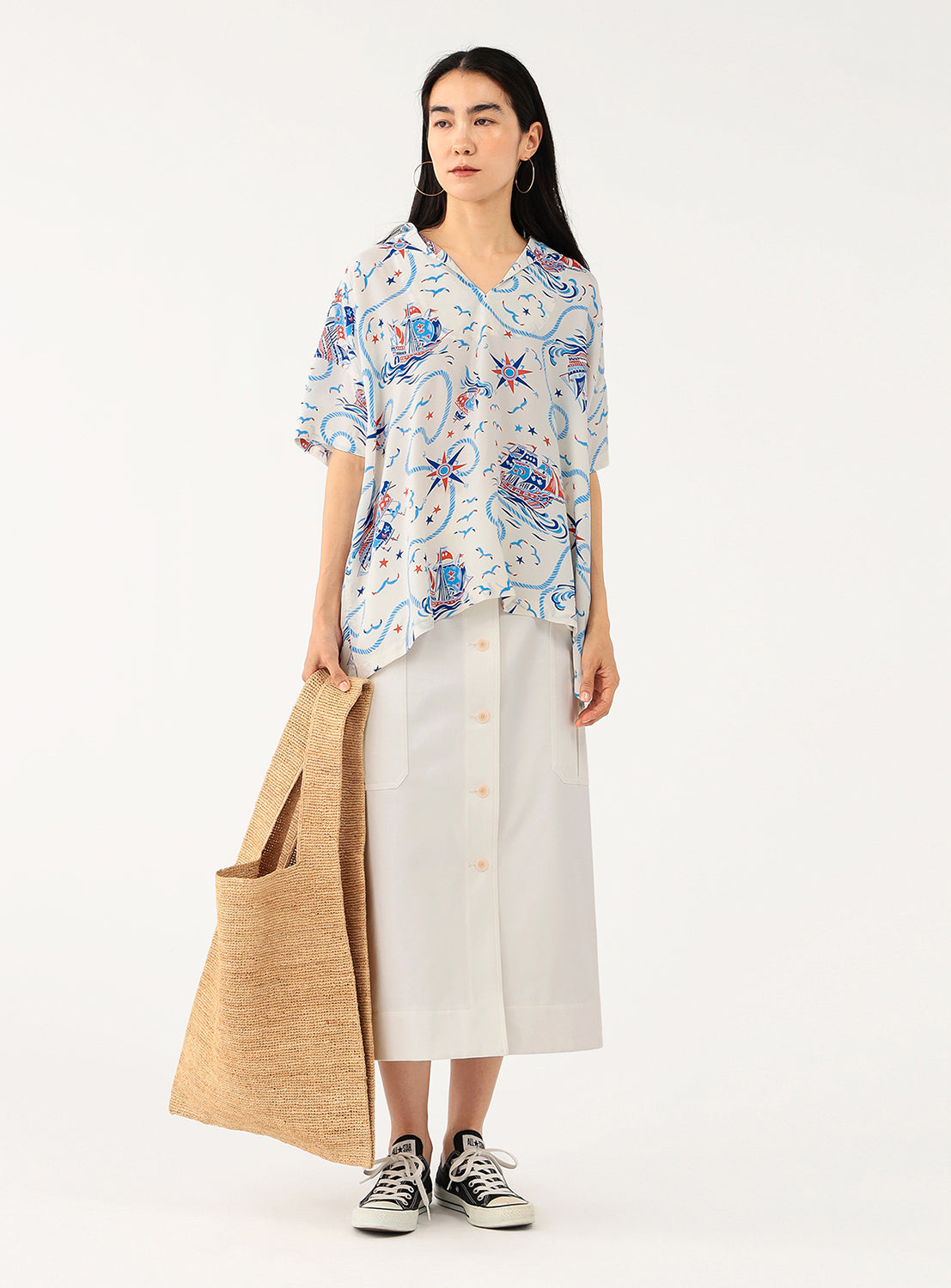 Full body shot of a model wearing a white patterned shirt, styled with a full-length skirt and a tote bag.