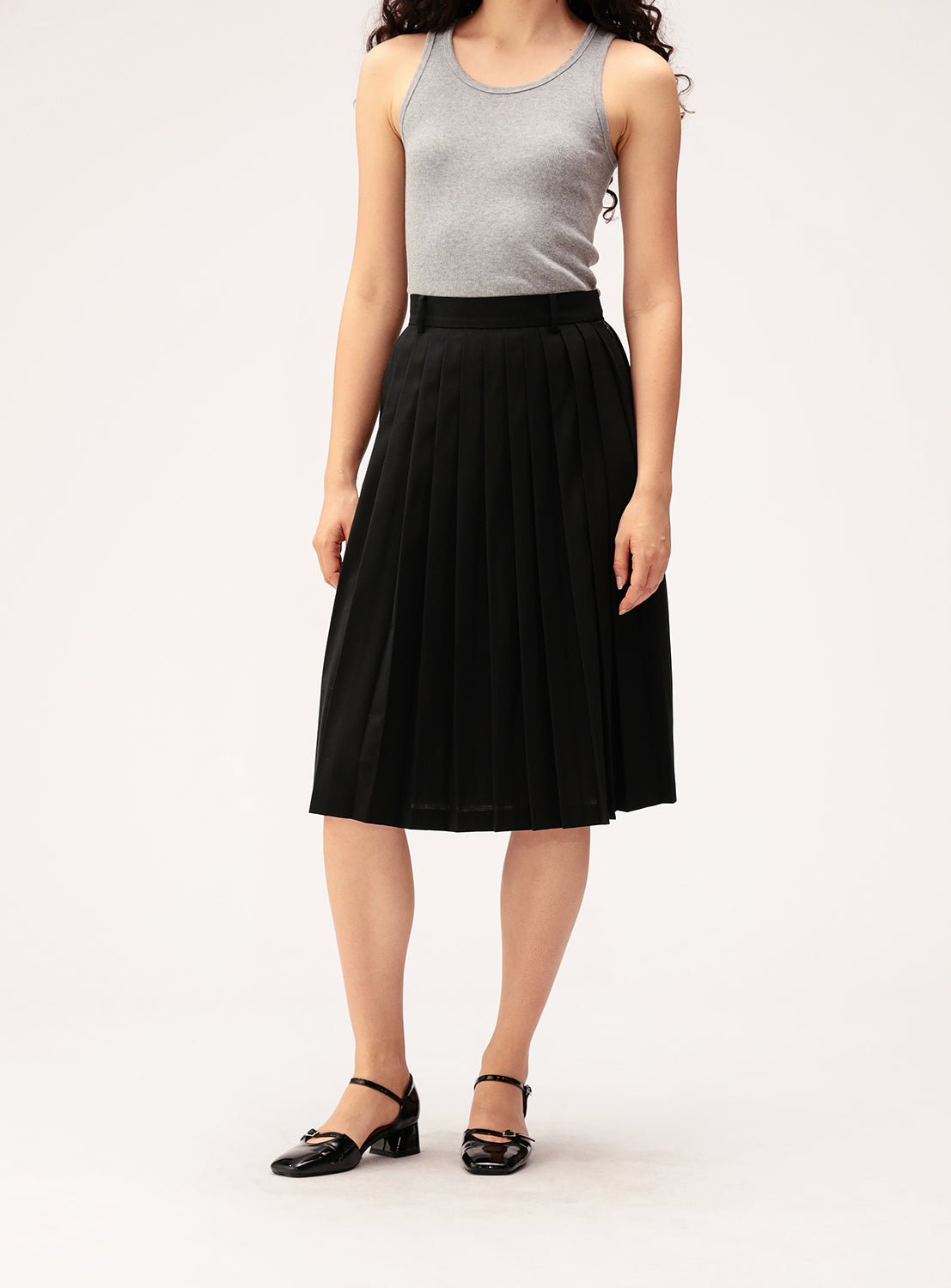 A person wearing a gray sleeveless top, the BEAMS BOY Mixed Pleat Skirt—a knee-length black skirt crafted from lightweight fabric—and black shoes stands against a plain light background.