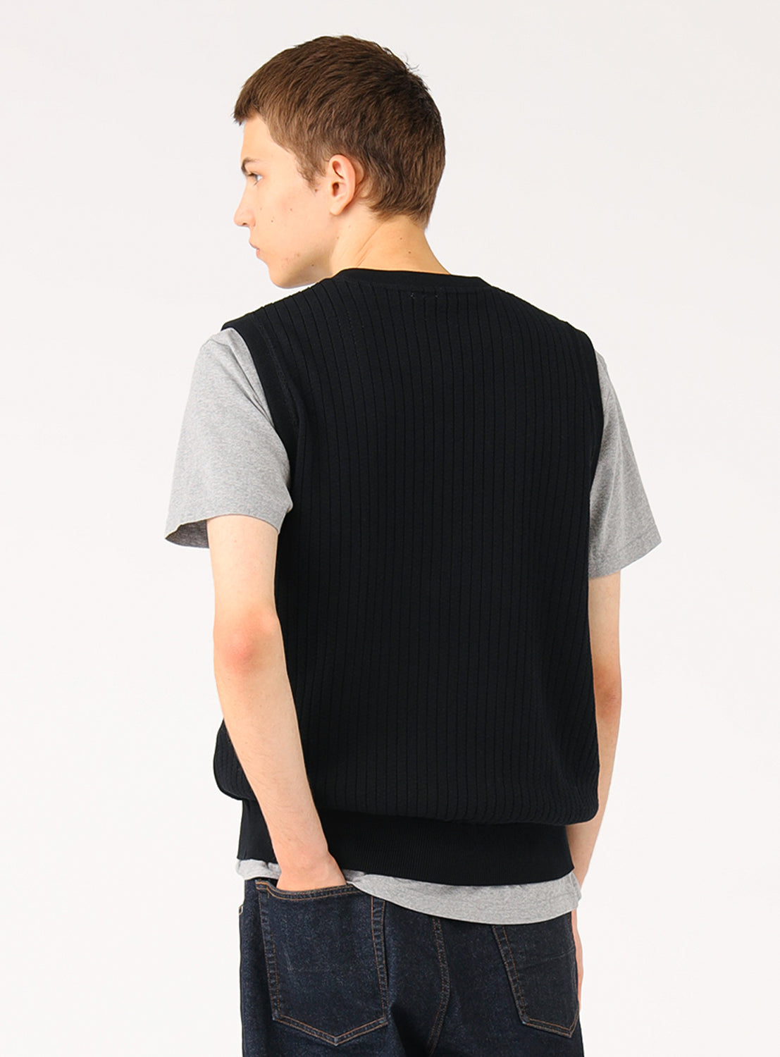 Model wearing a black ribbed knit vest over a grey t-shirt, back view, highlighting the vest's back texture.