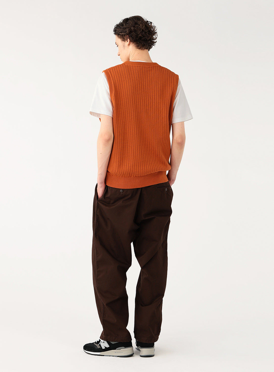 Model wearing a rust-colored ribbed knit vest over a white t-shirt, back view, highlighting the vest's back texture.
