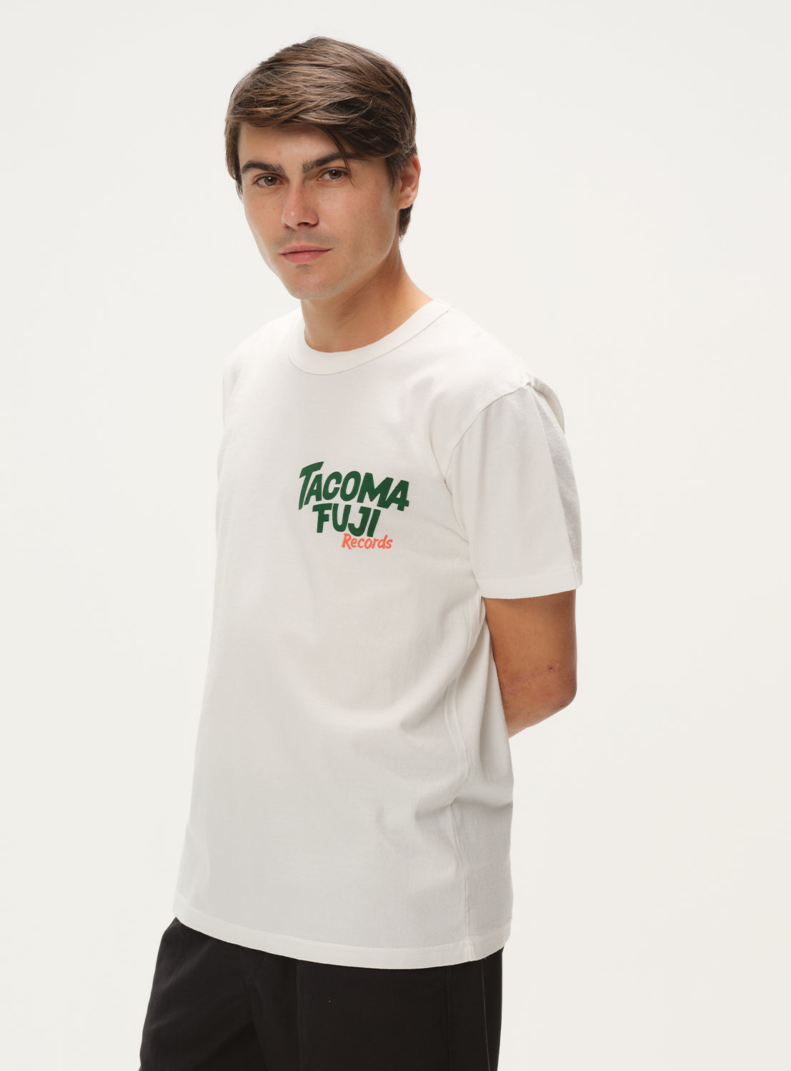 Model wearing a white t-shirt with "TACOMA FUJI Records" graphic and black shorts, side view, showing relaxed fit.