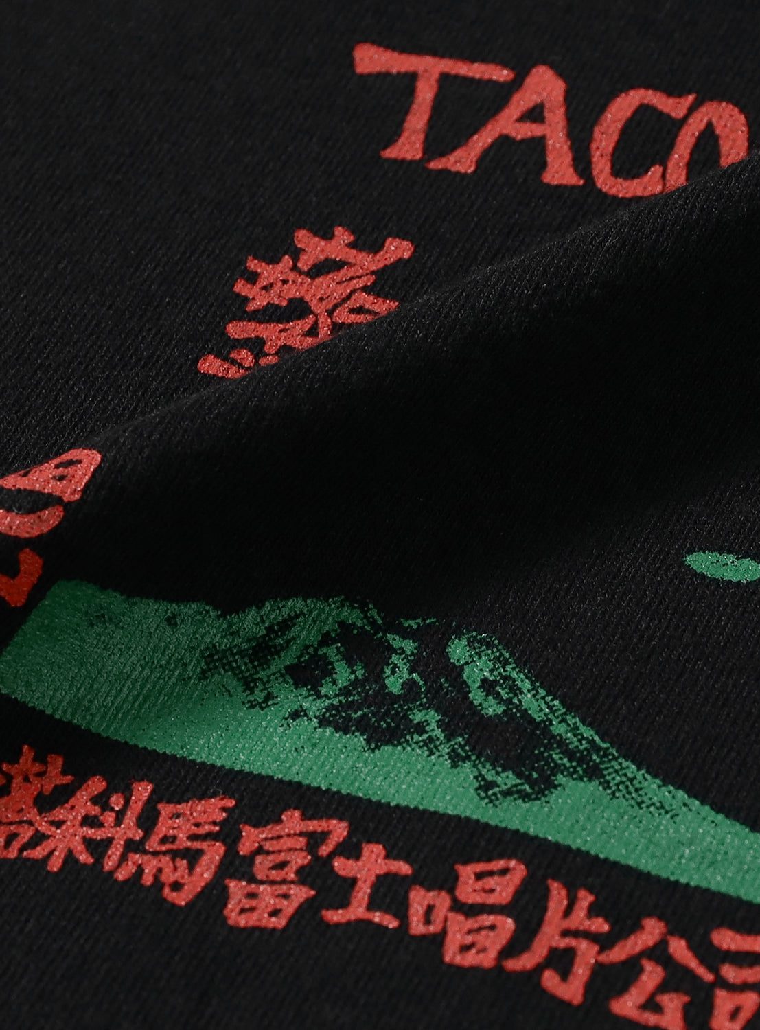 Close-up of black t-shirt fabric, detailing the red "TACOMA FUJI" graphic with green elements and Japanese characters.