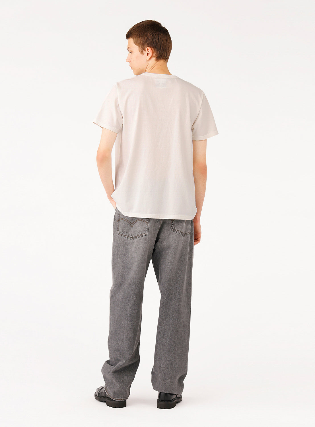 Model wearing a white t-shirt and grey pants, back view, showcasing the plain back of the shirt.