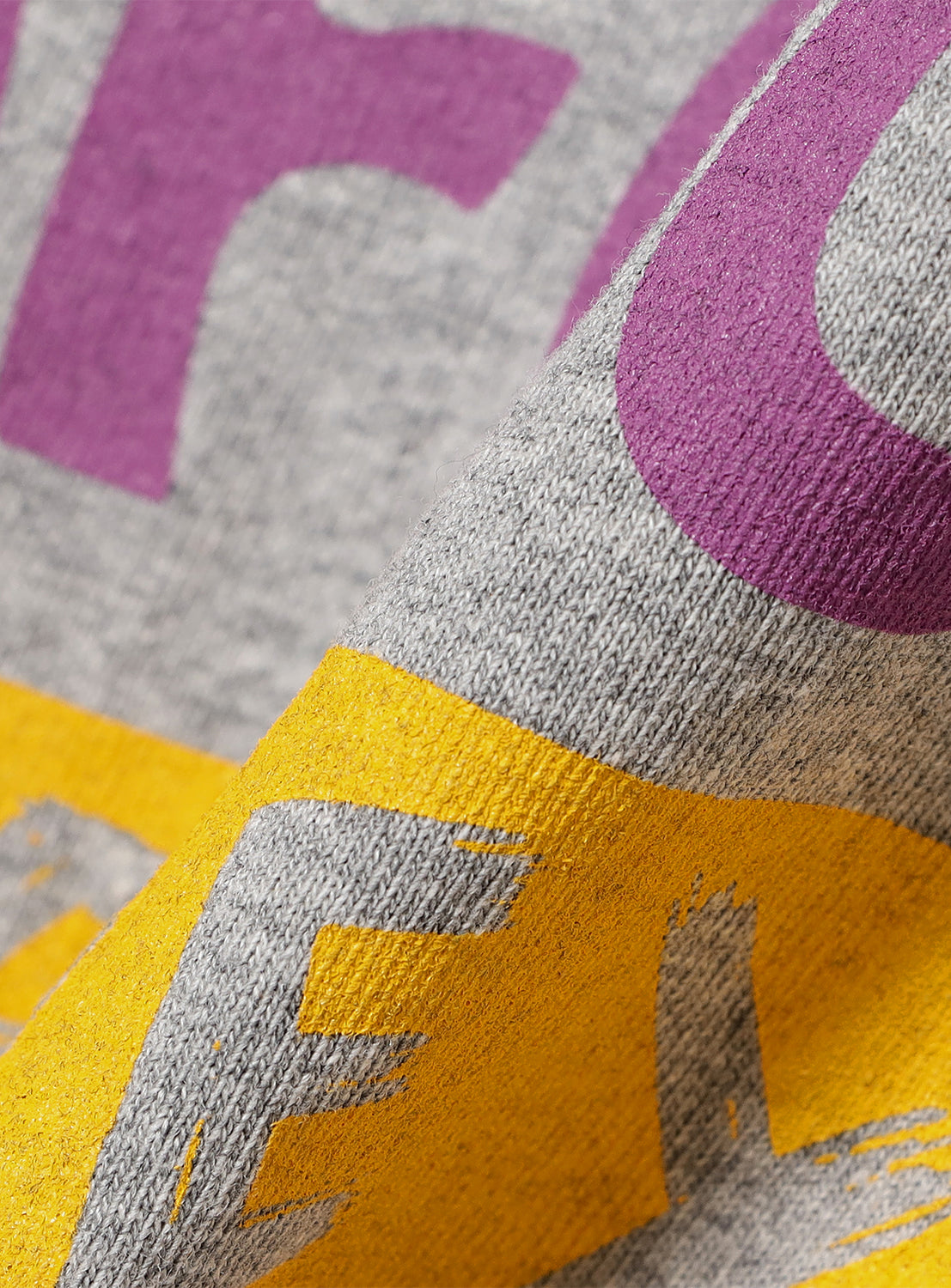 Close-up of light grey t-shirt fabric, detailing the vibrant purple and yellow "BIGFOOT PROJECT" graphic.