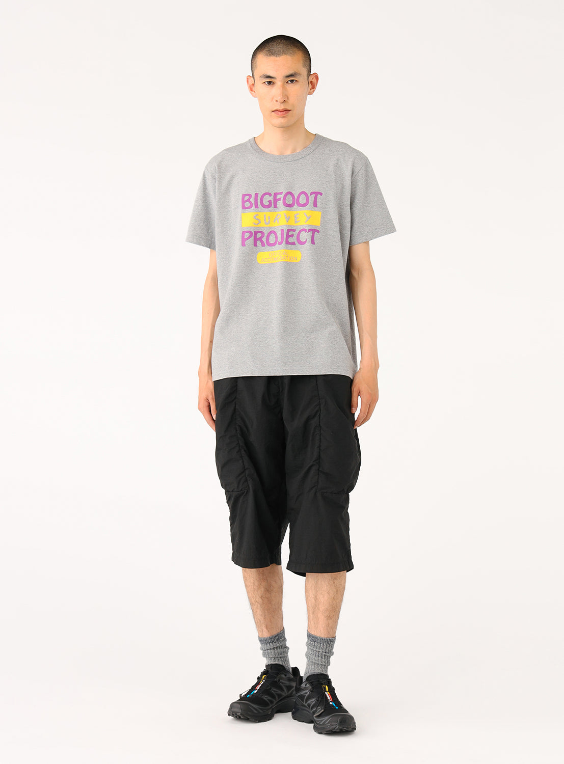 Model in a light grey "BIGFOOT PROJECT" t-shirt and black shorts, full front view, showcasing the complete outfit.
