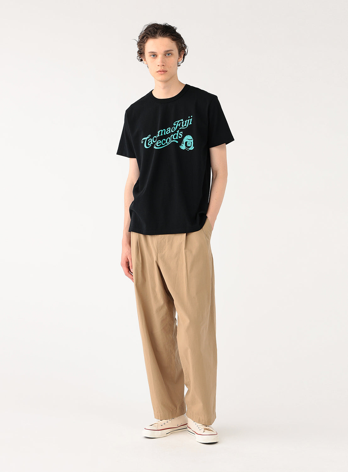 Model wearing a black t-shirt with "Tacoma Fuji Records" graphic and khaki pants, side view, showing casual fit.