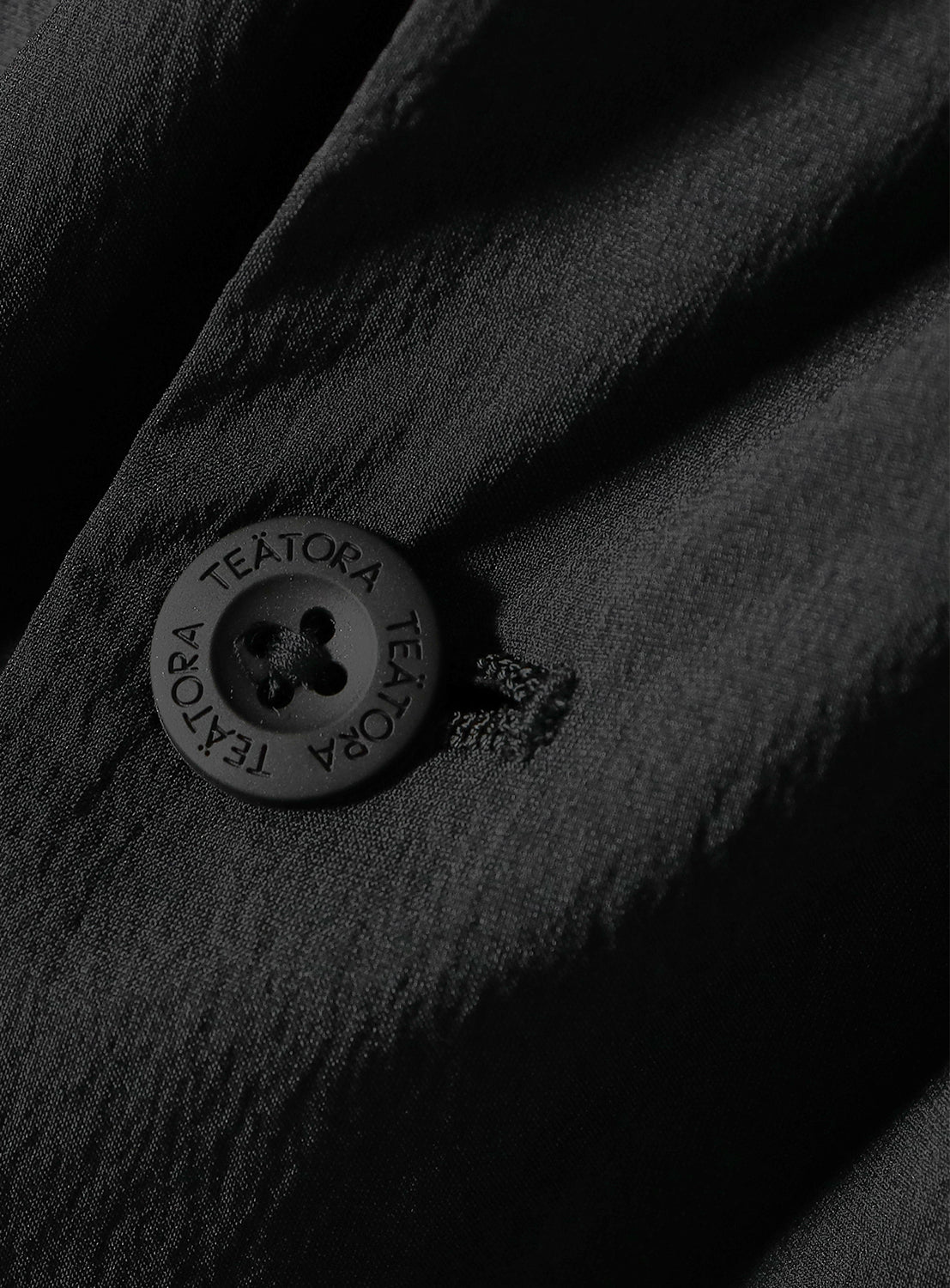 Close-up of a black shirt button on DOCTOROID (DR) fabric, detailing the texture and button design.
