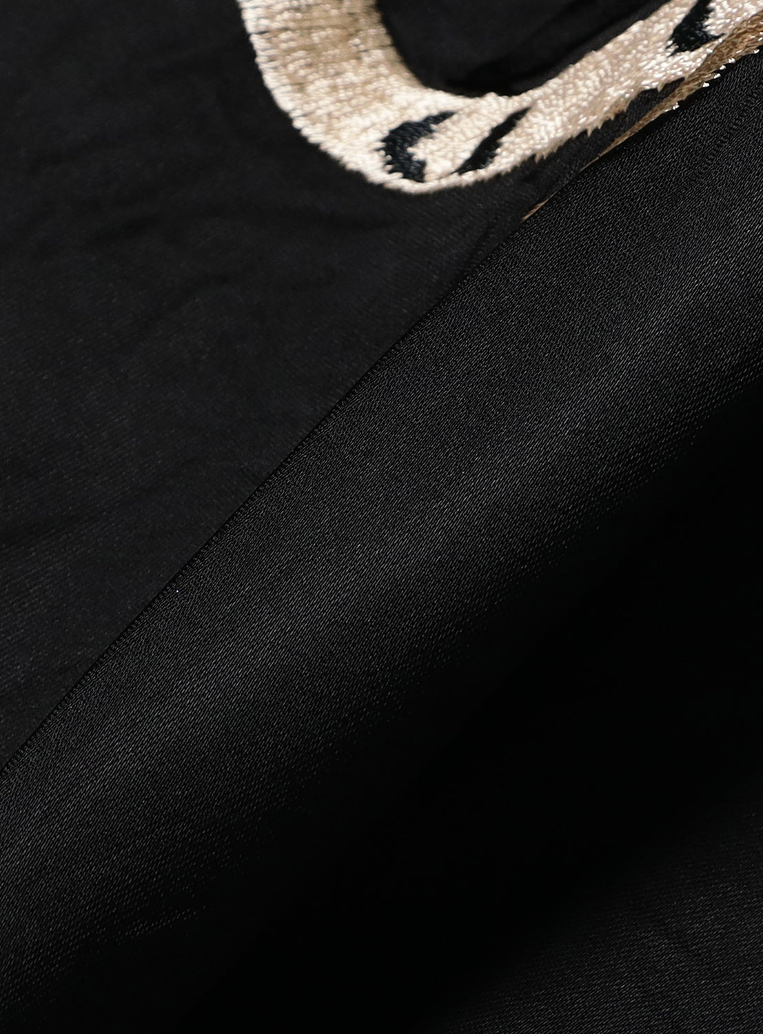 Close-up of black fabric from the Late 1940s Style Acetate Souvenir Jacket KOSHO & CO. Special Edition “WHITE TIGER” × “JAPAN MAP” by TAILOR TOYO, featuring beige and black embroidery with detailed stitching and smooth texture.