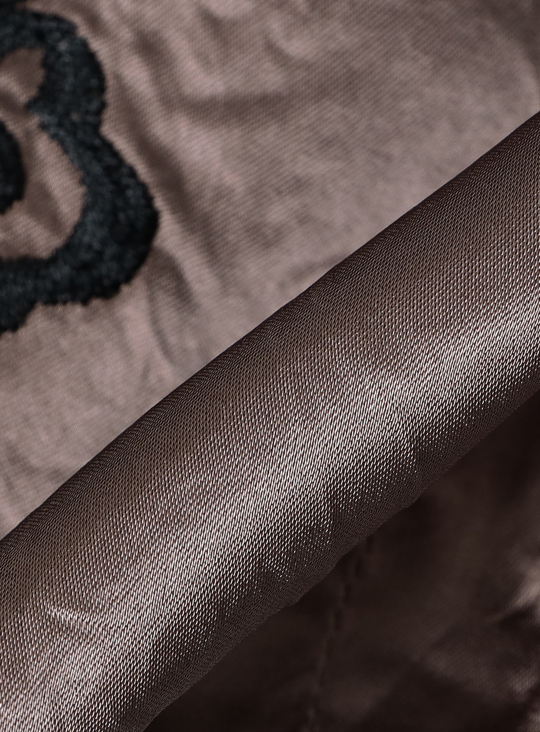 Close-up of brown, textured acetate fabric from the TAILOR TOYO Late 1940s Style Souvenir Jacket KOSHO & CO. Special Edition “WHITE TIGER” × “JAPAN MAP”, showing raised black embroidery and a neatly folded edge.