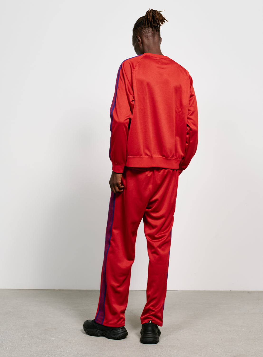 Back view of a model wearing a red track pants with blue/purple stripes on the side.