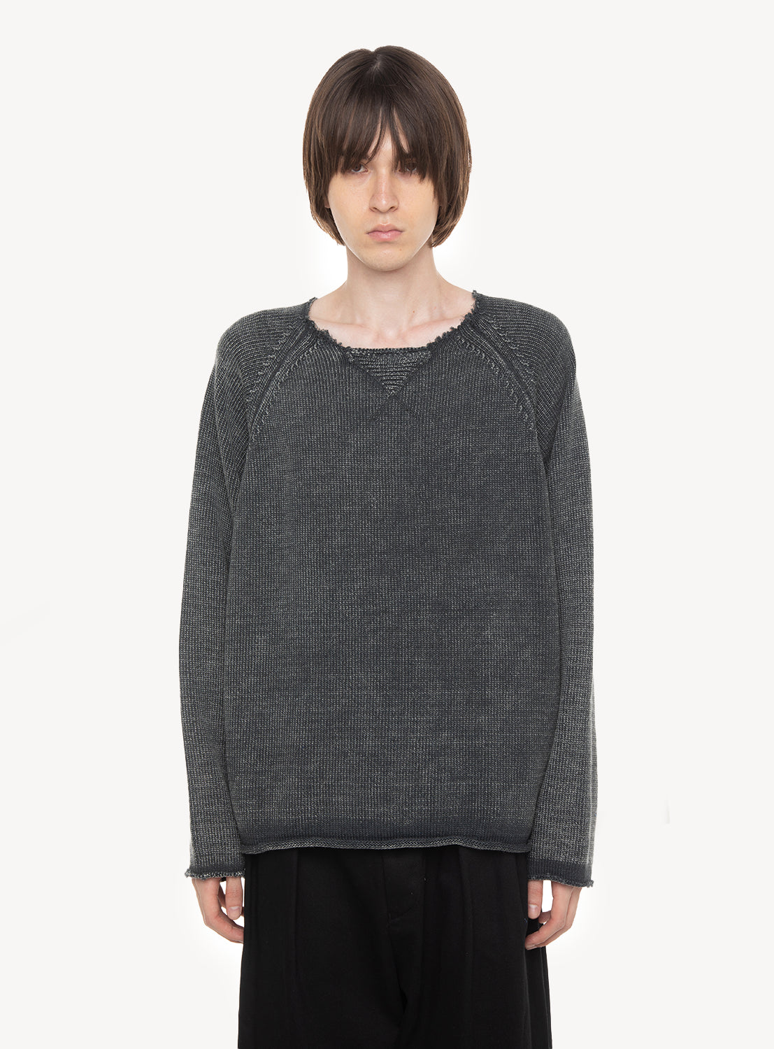 A person with short brown hair wears the DAIRIKU Vintage Washed Pullover Knit Sweater—a loose, dark gray knit made from 100% cotton—paired with black pants, standing against a plain white background with a neutral expression.