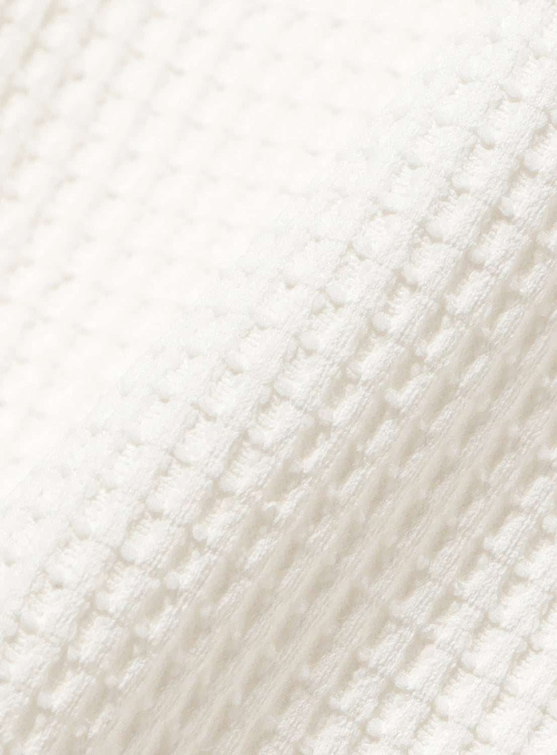 Close-up of the BEAMS Stretch Waffle T-Shirt in white, featuring a stretchable synthetic waffle fabric with a textured waffle weave pattern shown at an angle. The lighting highlights the raised squares and soft folds in the material, emphasizing its quick-drying and moisture-wicking qualities—perfect for a performance T-shirt.