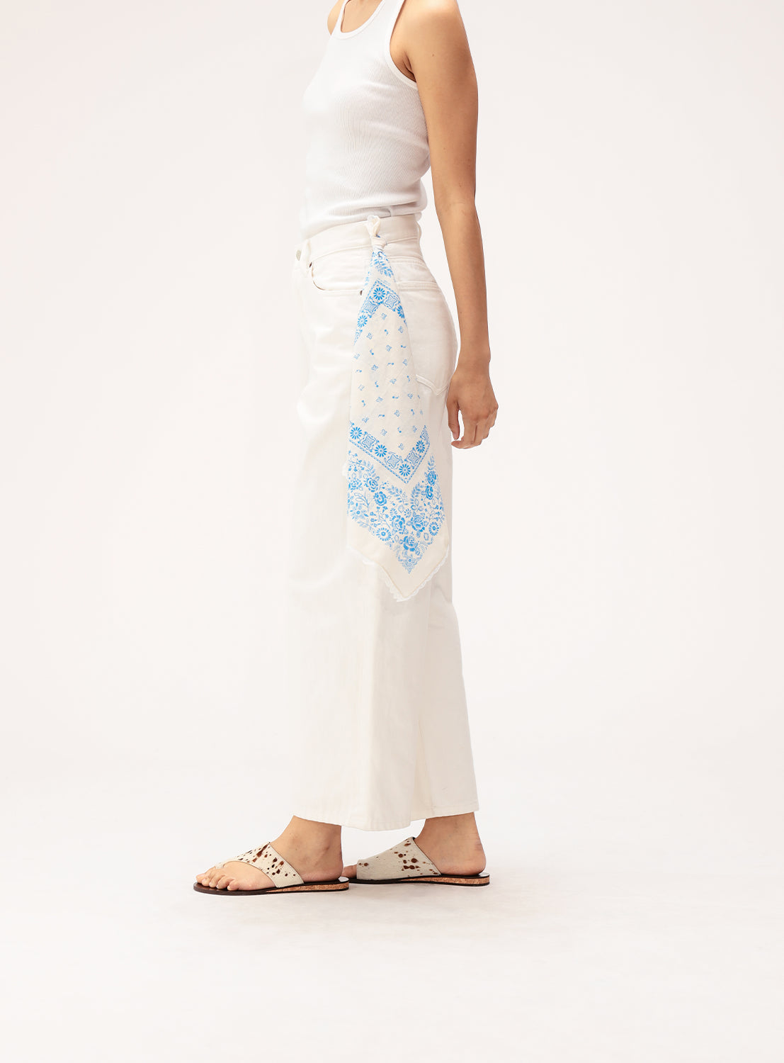 A person wearing a white tank top, white wide-leg pants, flat sandals, and the BEAMS BOY 2-Way Floral Bandana in blue tucked into their pocket stands against a plain white background.