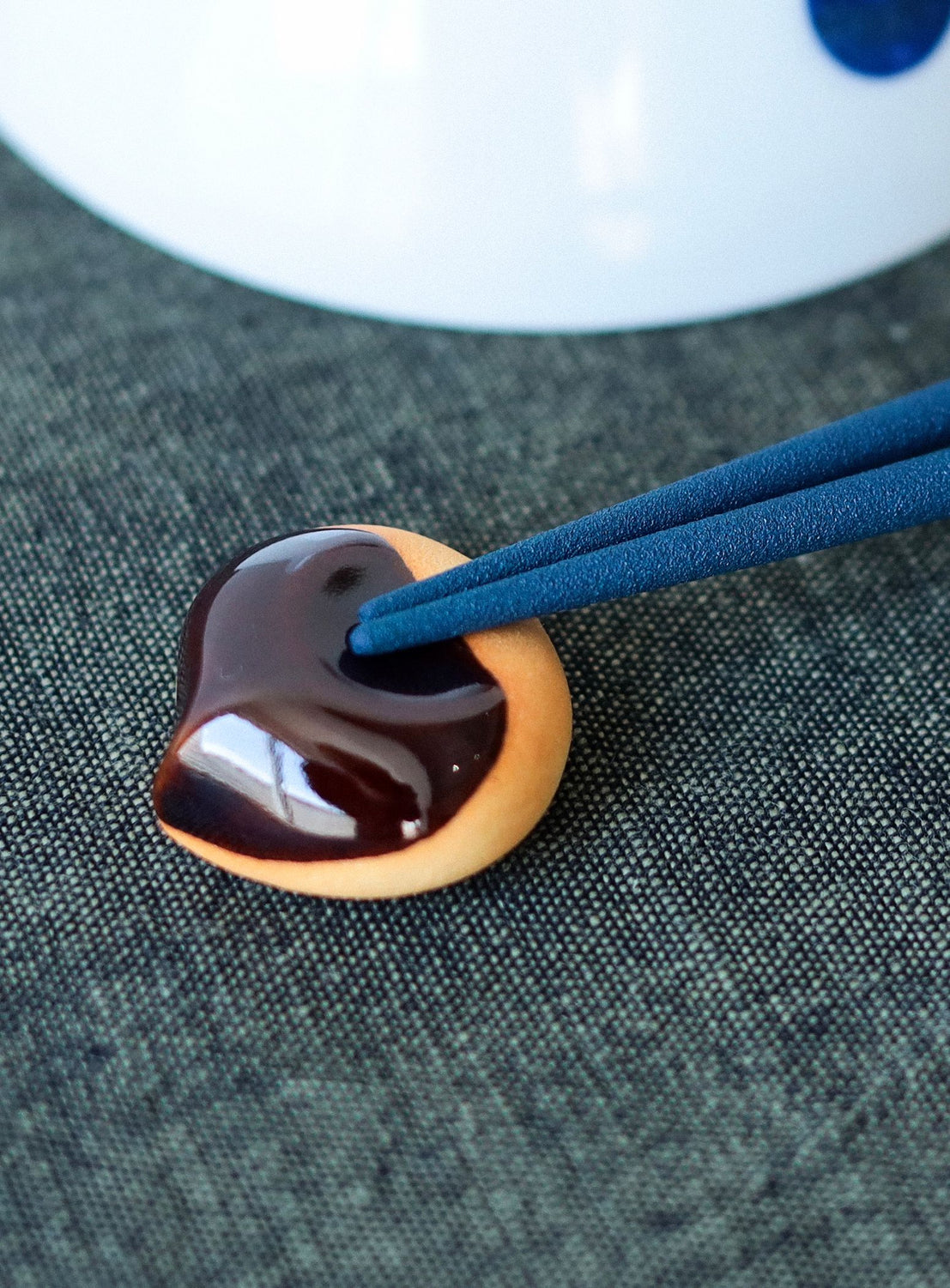 Chocolate-covered cookie chopstick rest with blue chopsticks on a textured surface