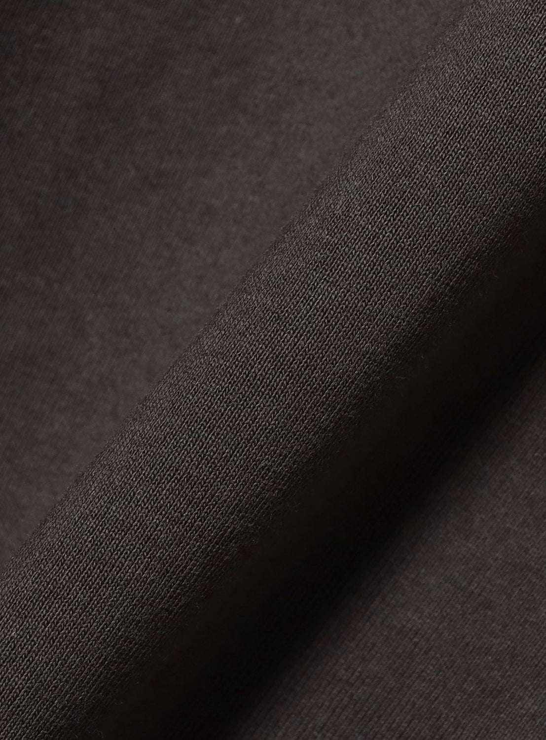 A close-up of dark brown, textured fabric with a visible weave and soft diagonal fold, evoking the comfort of the CHAMPION [Exclusive] Mock Layered Long-Sleeve T-Shirt.