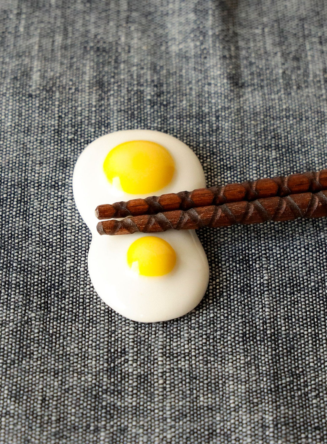 Two small round eggs with yellow yolks on a textured surface with wooden chopsticks.