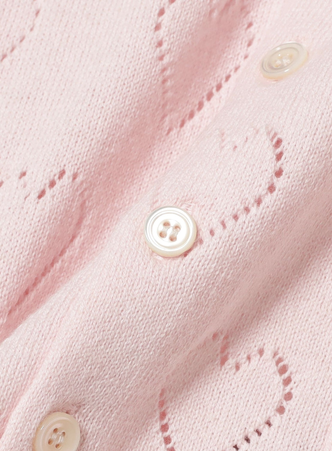 Close-up of the TTT MSW Flower Embroidery Knit Shirt, featuring pale pink merino wool fabric, white buttons, and a subtle heart-shaped openwork knit pattern.