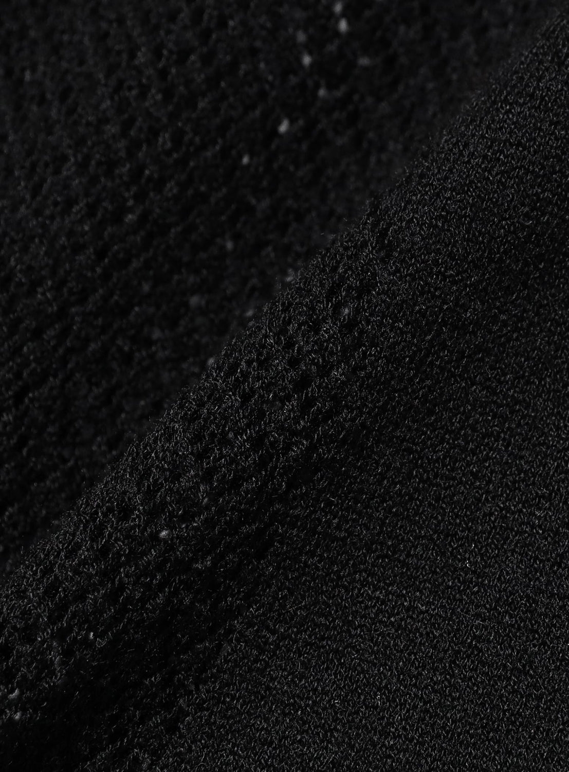 Close-up of black textured fabric from the BAL Ventilation Mesh Knit Zip Short Sleeve Polo Shirt, featuring two sections: one smoother and one with a rougher, looped surface, divided diagonally across the image. The subtle contrast highlights the refined finish typical of high-gauge knit polo designs and showcases the tactile appeal of this innovative merino wool blend.