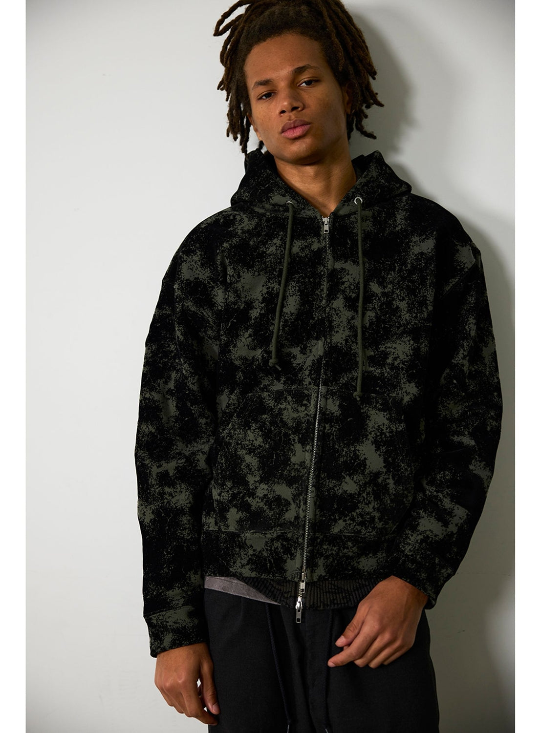 A person wearing a BEAMS Flocked Planet Motif Full-Zip Hoodie, an oversized vintage-inspired piece with a black full-zip closure and an olive green mottled pattern.