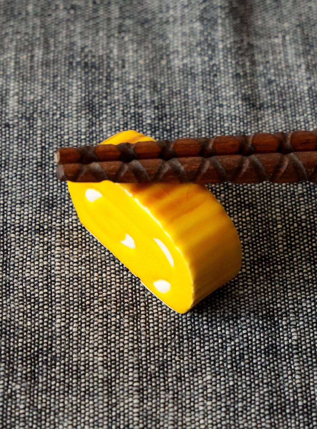 Yellow ceramic chopstick rest with brown wooden sticks on a gray textured fabric background