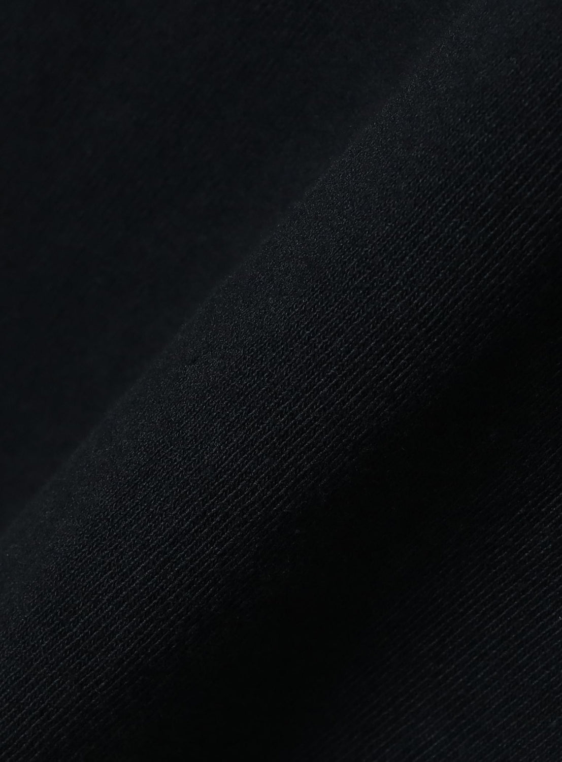 Close-up of a folded piece of black fabric from the BEAMS T Tyrrell Winston - Sign T-Shirt, highlighting its fine texture and weave pattern with subtle light and shadow.