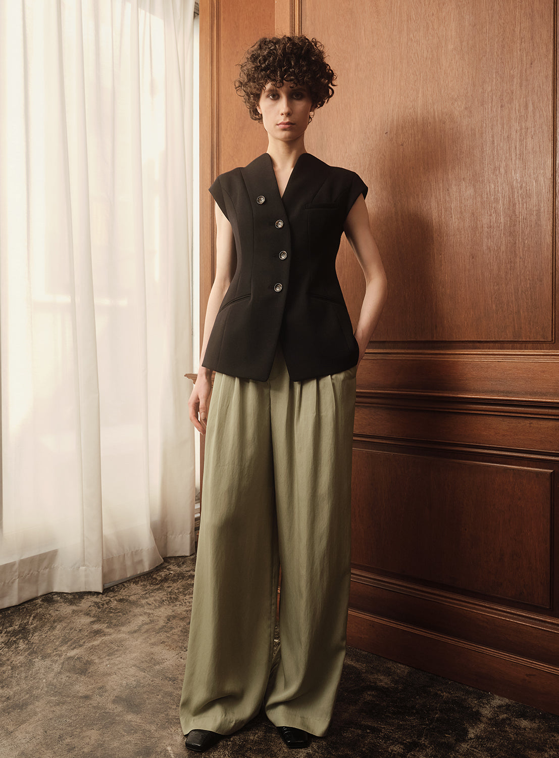 A female model wearing a dark navy tailored cap sleeve vest with gold buttons.