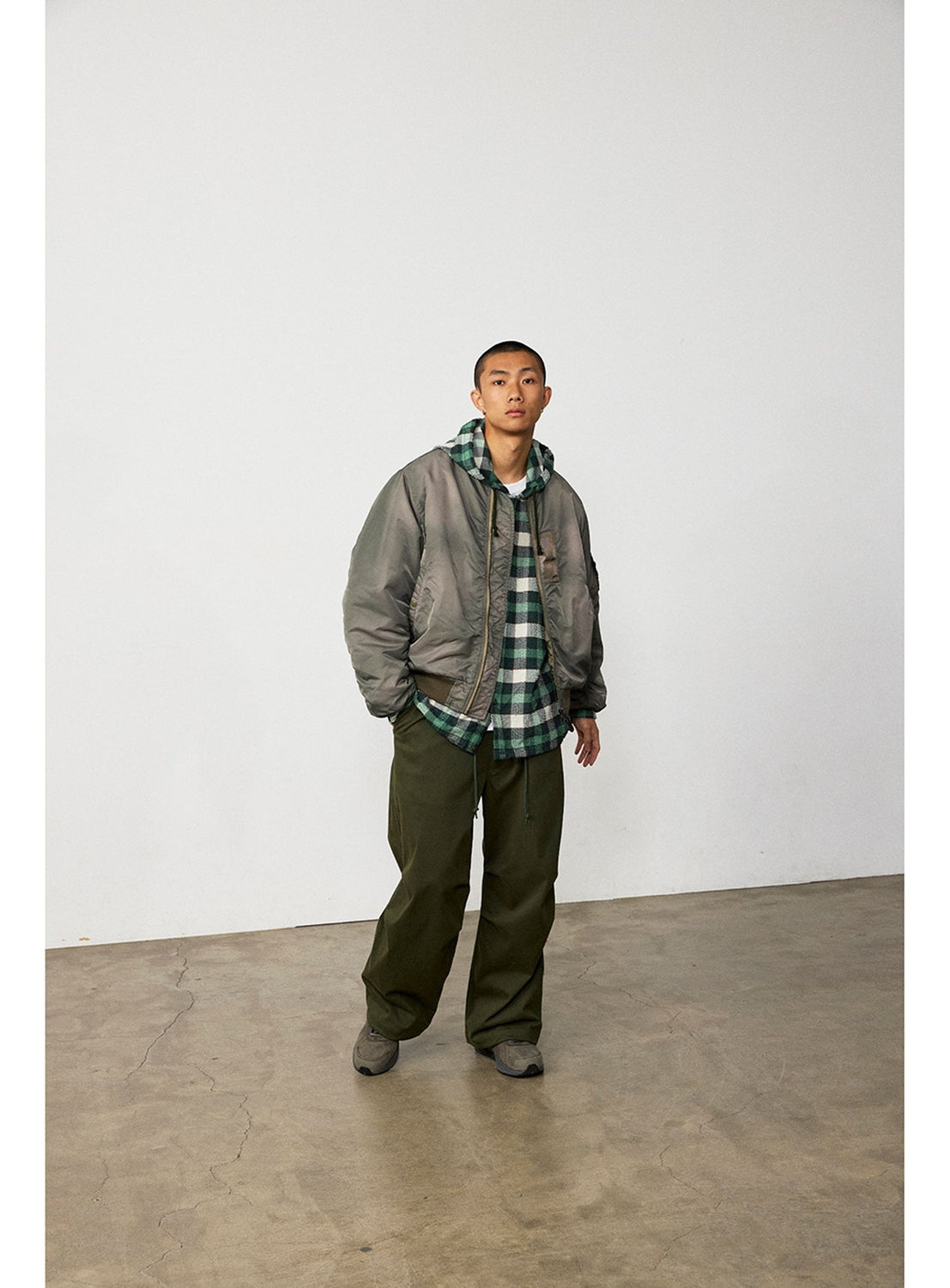 A person wears a grey bomber jacket over a green and white BEAMS Bouclé Flannel Hooded Shirt with a textured check pattern and olive green trousers.