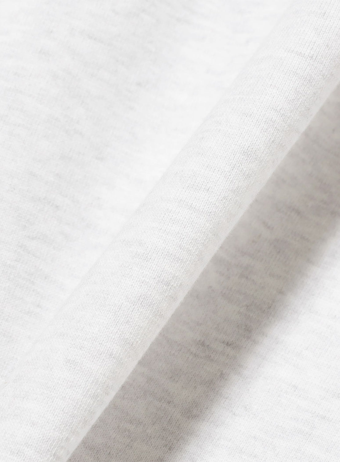 Close-up of soft, light grey or white fabric with a distinct diagonal fold, capturing the premium texture typical of TTT MSW streetwear essentials—ideal for the Wave Logo Ringer T-Shirt.