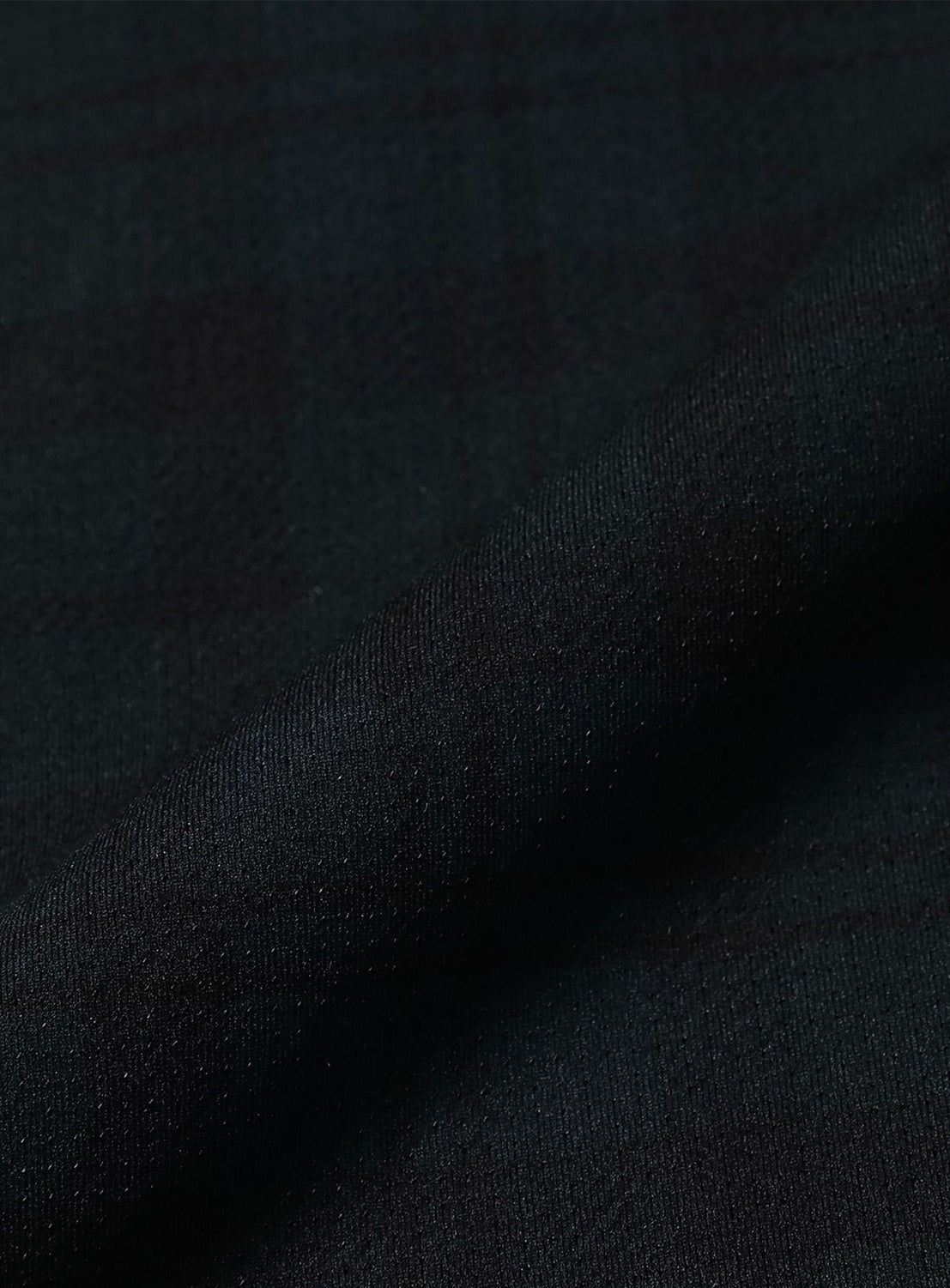 Close-up of dark, textured fabric with a subtle plaid pattern and a diagonal fold, highlighting the fine weave and soft sheen—exemplifying the BEAMS Wide Straight Fit Dynamic Dry Easy Pants, the perfect material for technical performance wear.