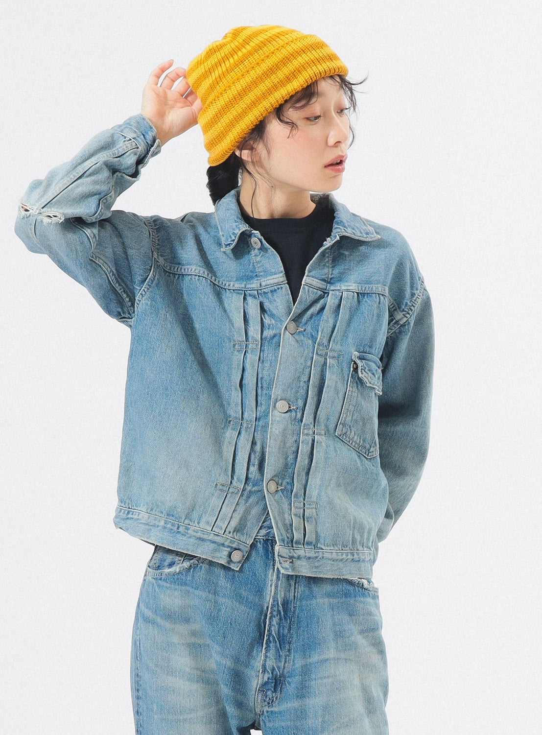 Person wearing a denim jacket and yellow beanie on a white background