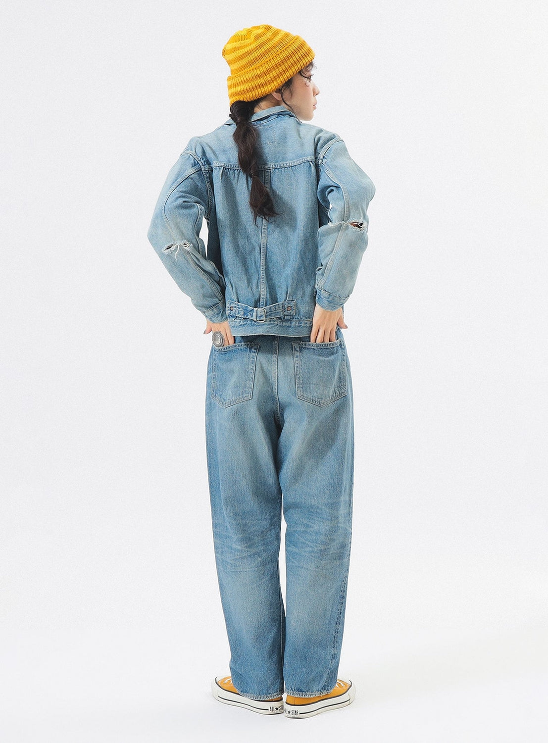 Person wearing a denim jacket and jeans with a yellow beanie on a white background