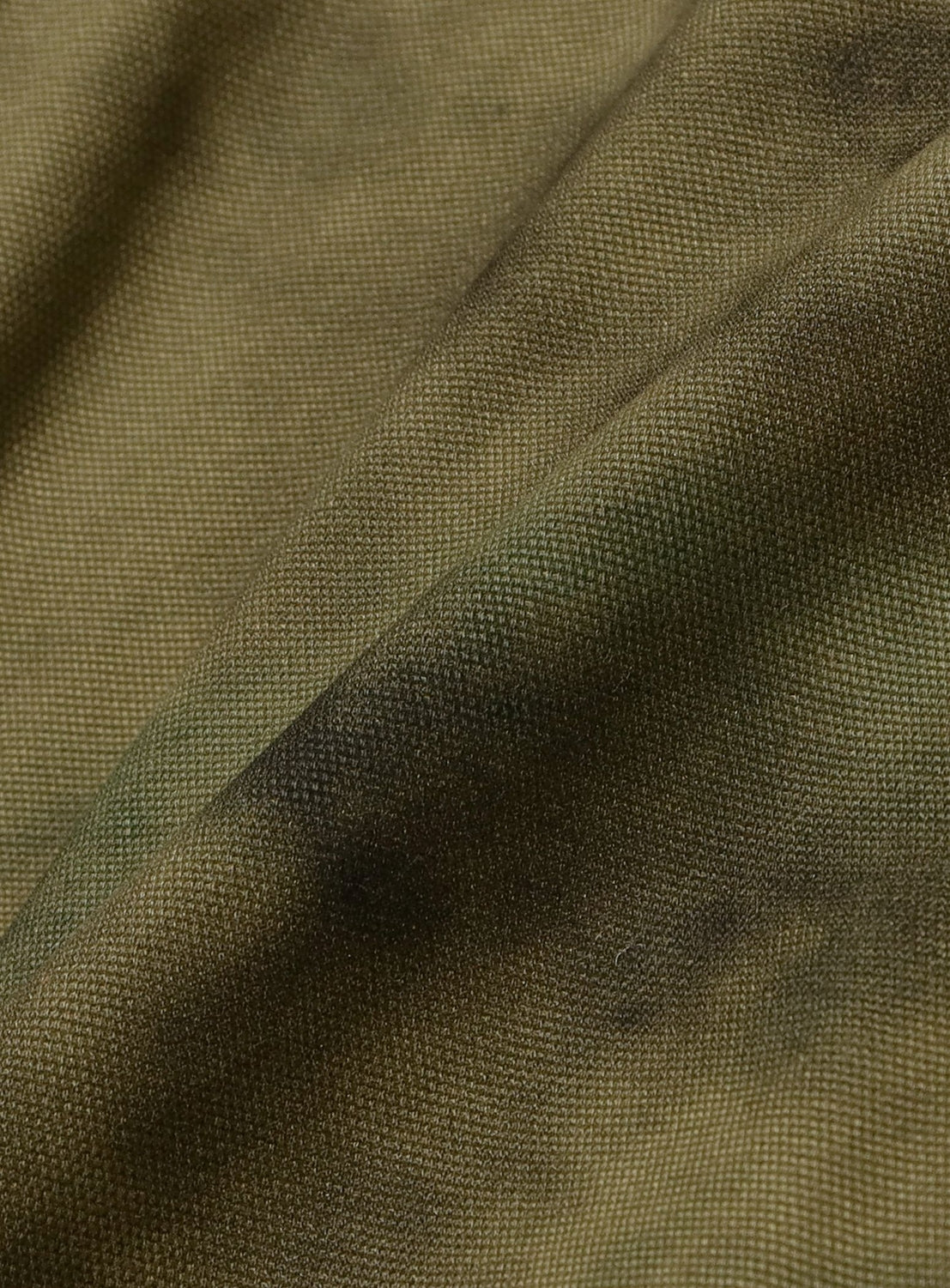 Close-up of the TTT MSW Camouflage Swing Top Jacket's olive green cotton twill fabric, featuring a textured weave with subtle darker patches, gentle folds, and soft shadows.